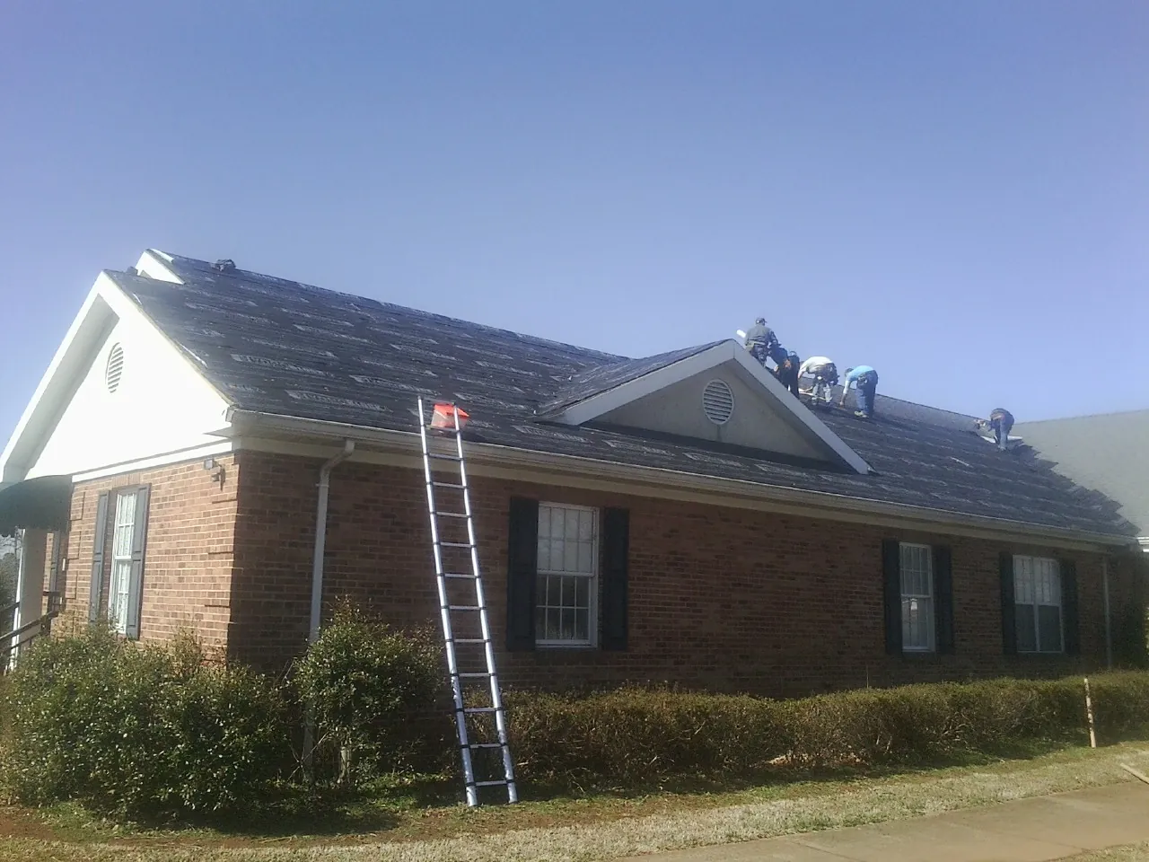 Crew tearing shingles off a brick ranch roof with a ladder set — Emergency Roof Repair work by our crew in Mount Sterling