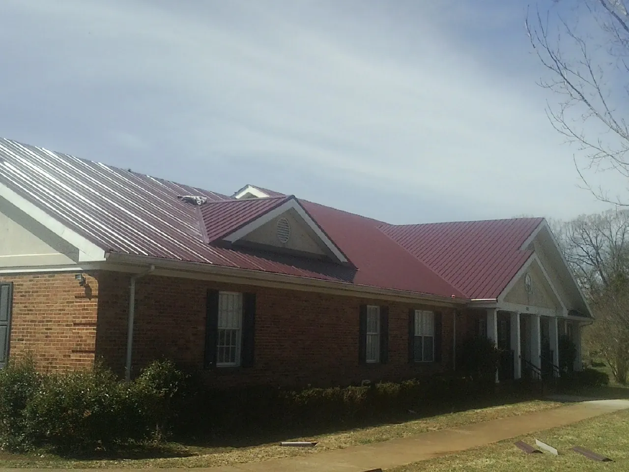 Red metal roof with gabled entries on a long brick building, from a Hail Damage Roof Repair job in Mount Sterling