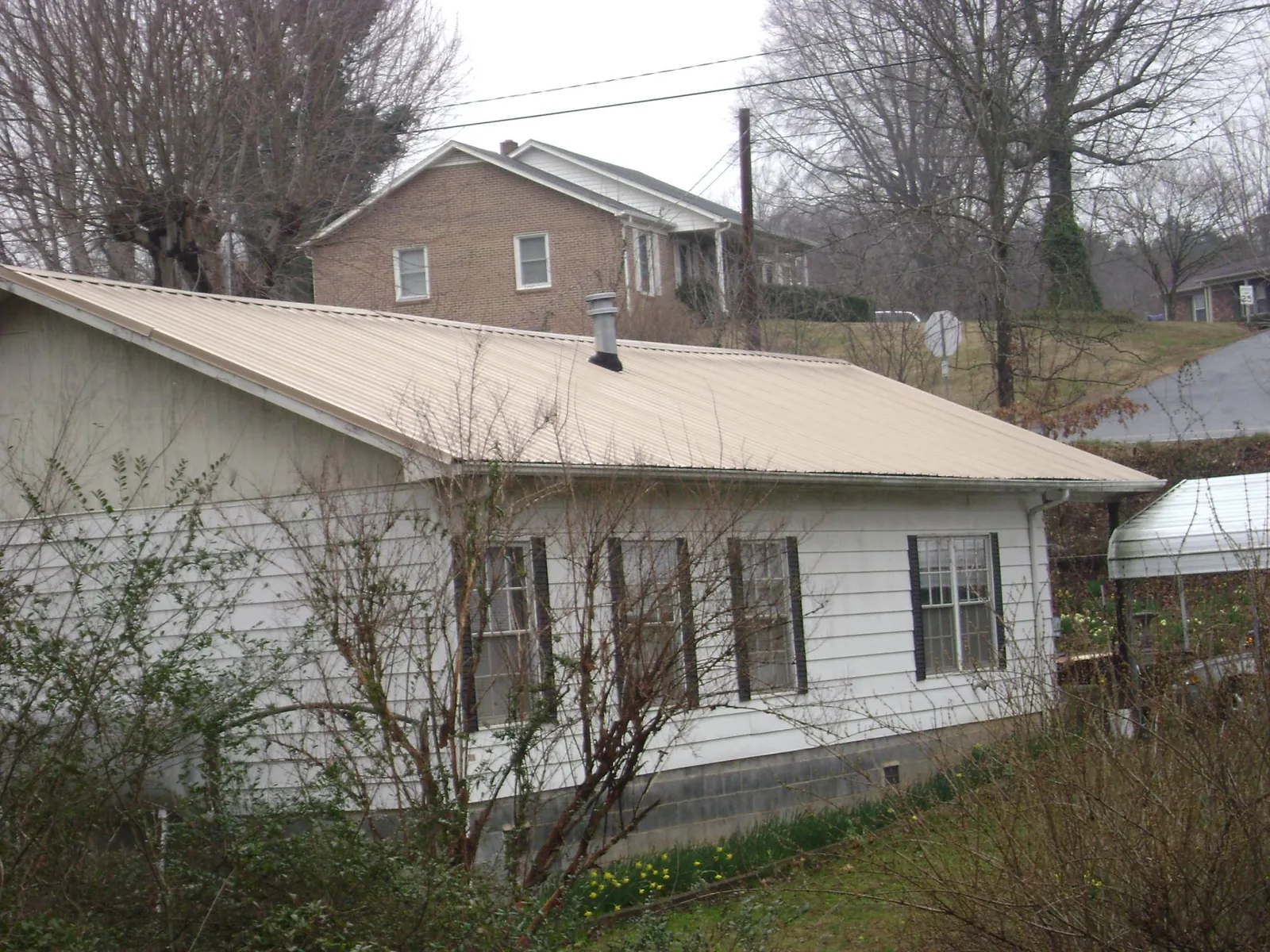 Tan metal roof on a white sided house set into a hillside — Commercial Roofing by Roofing Brothers in Mount Sterling